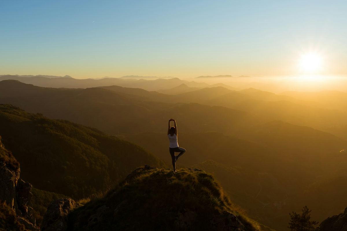 A person doing a yoga pose on a hilltop at sunrise